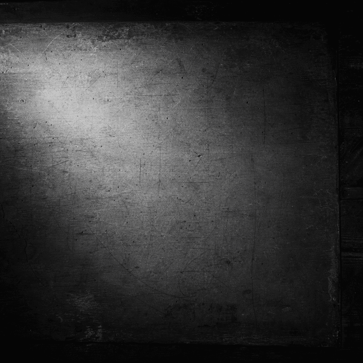 An overhead photographic view of an old worn artist work-table covered with faint pencil marks, lit by a soft pool of dim light from above-left, deep dark wood at the edges. The substrate the canvas overlay paints onto.