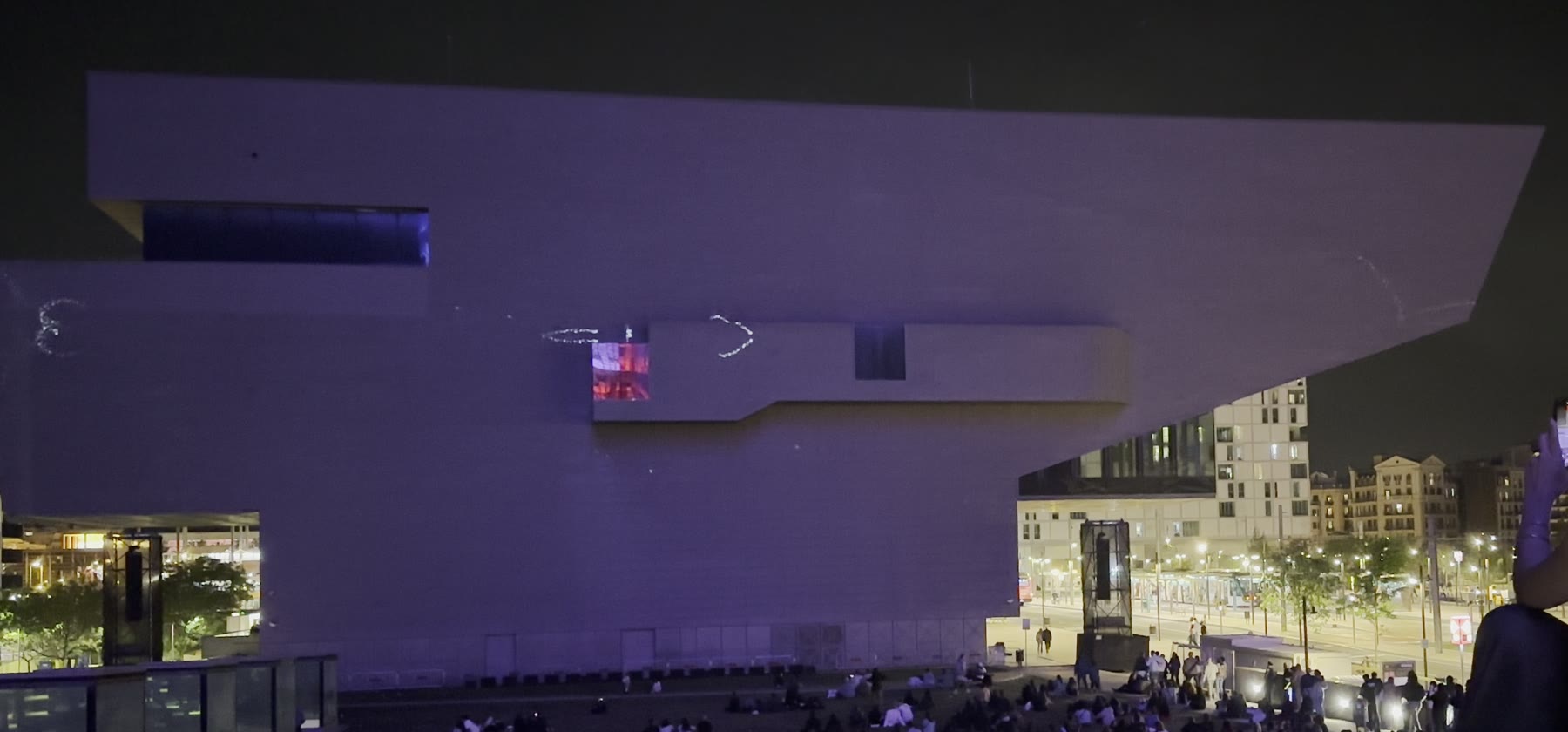 EMPREMTA — first phase. The dark purple facade of the Disseny Hub with a few faint, handmade-looking silver marks beginning to appear across the cantilever.